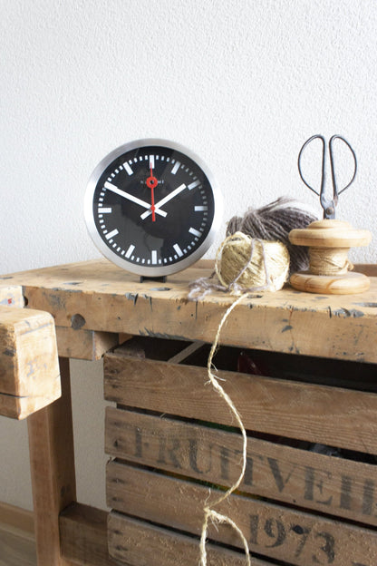 Black aluminum NeXtime Station Stripe wall or table clock with a sleek, modern design and minimalist striped pattern.